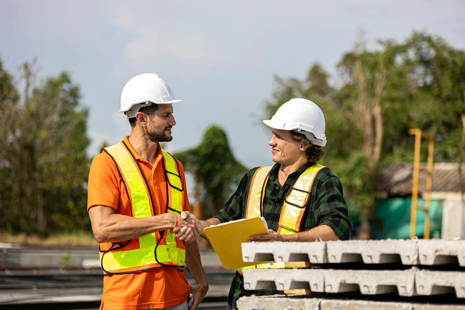 Two builders in hard hats and safety vests shaking hands on a job site