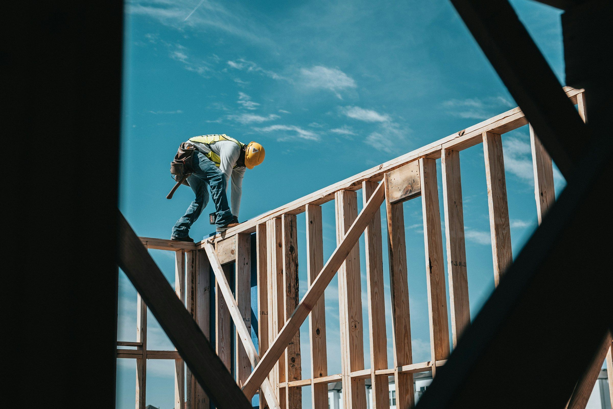 Carpenter in a hard hat working on the wood framing of a new home against a clear sky